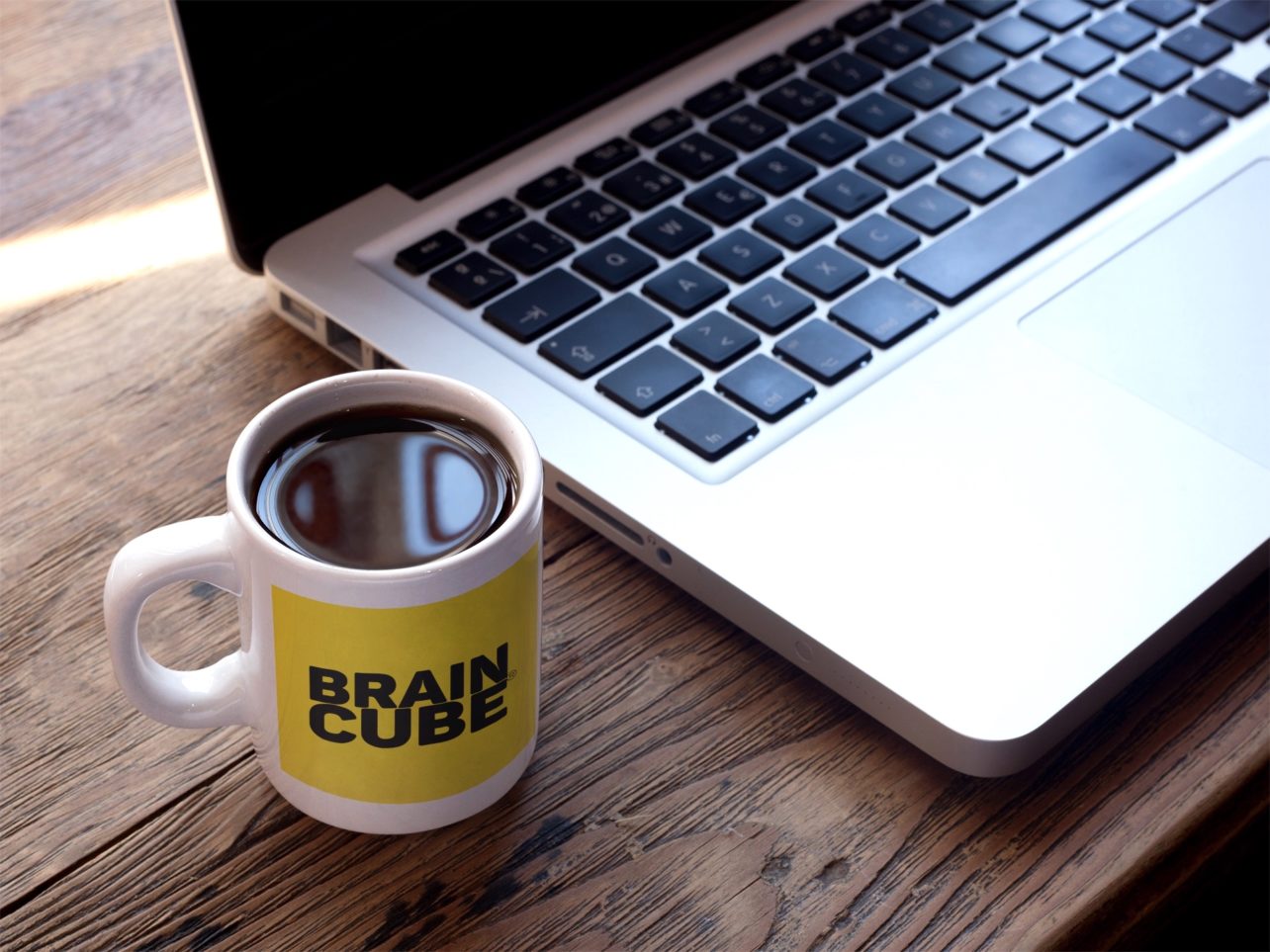 Cup of coffee with Braincube logo next to laptop