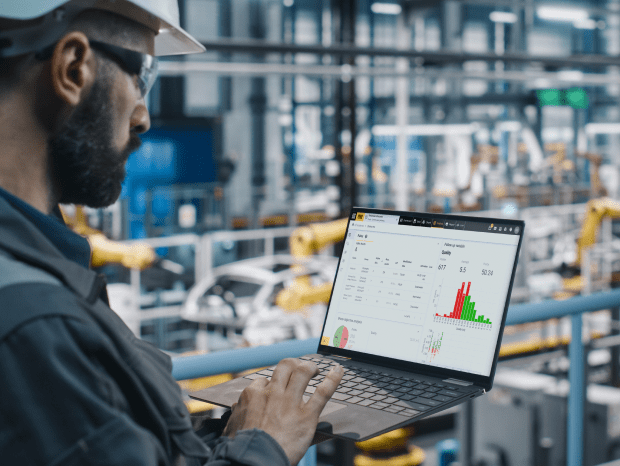Man standing inside a factory holding laptop with data on it